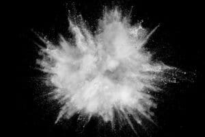 A burst of combustible dust explodes against a black background, creating a cloud of fine particles with dynamic and sharp edges, resembling an abstract starburst pattern.