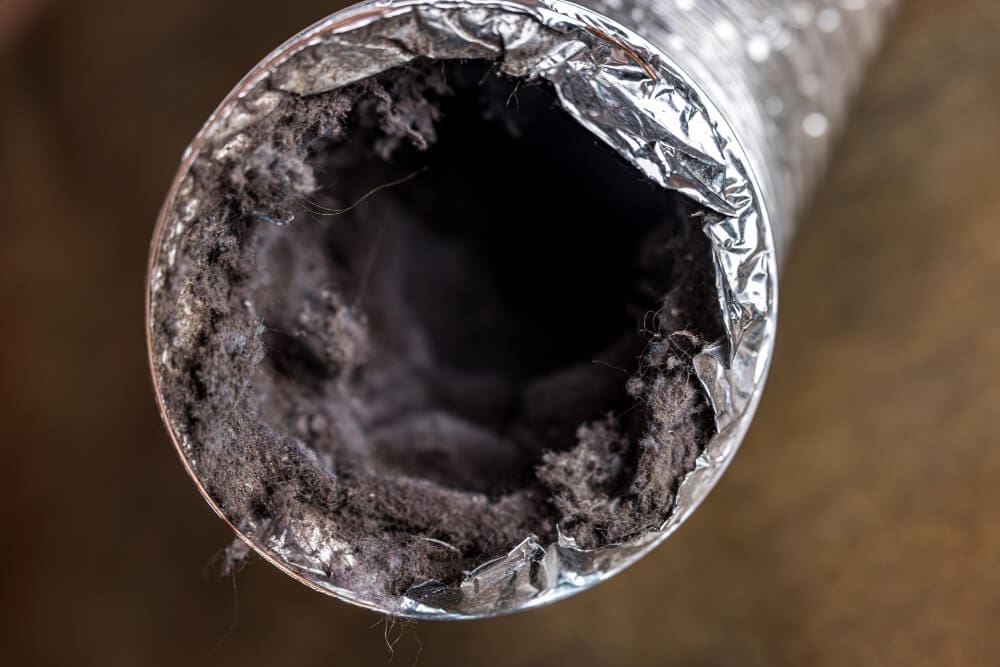 Close-up of a dryer vent hose clogged with dark lint and debris, highlighting the urgent need for cleaning. The image shows a partially blocked opening, underscoring potential fire hazards and inefficiency in venting systems.