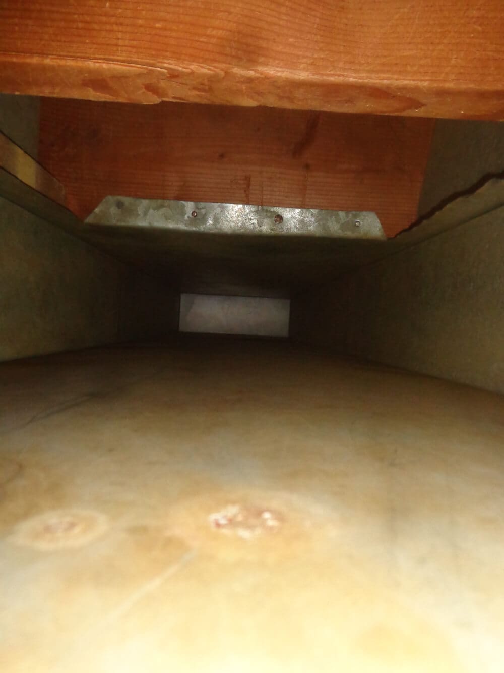 A view inside an air duct reveals its metal walls and a rectangular opening at the far end, highlighting the need for duct cleaning. The image captures the interior structure bathed in light, emphasizing areas where dust and debris may accumulate.